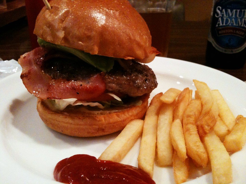 Hamburguesa con panceta y papas fritas en plato blanco
