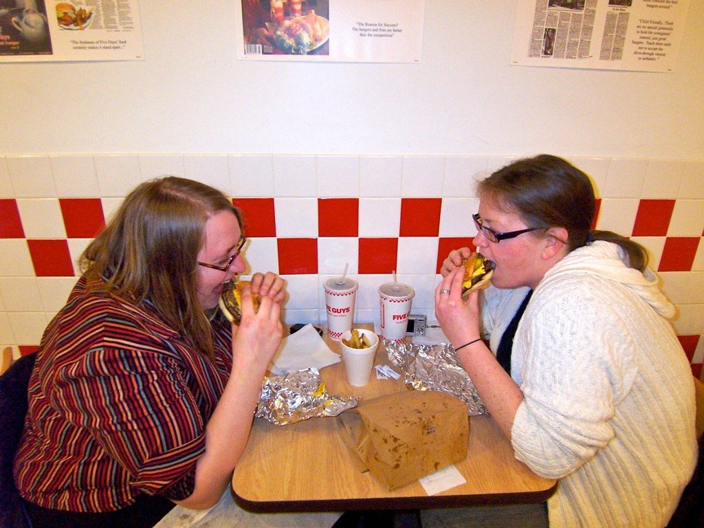 Dos amigas comiendo hamburguesas en una mesa del local